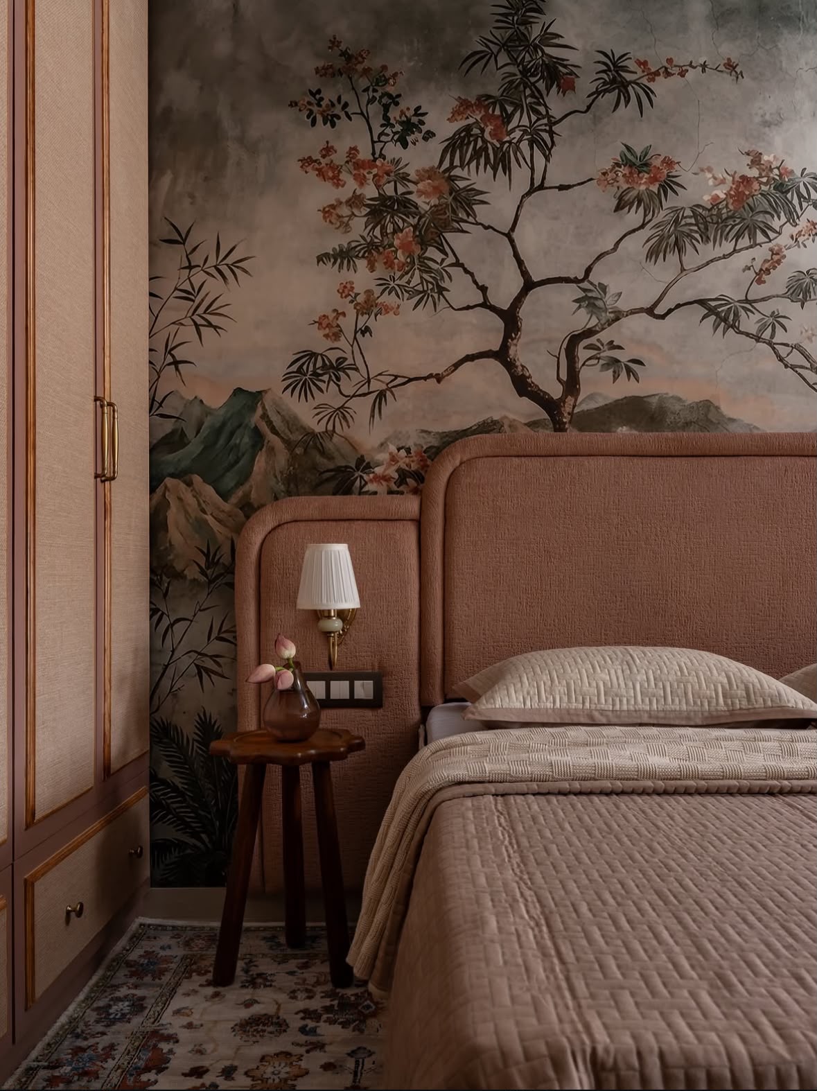 Bedroom with a painted landscape wallpaper, an upholstered headboard and a brass wall light