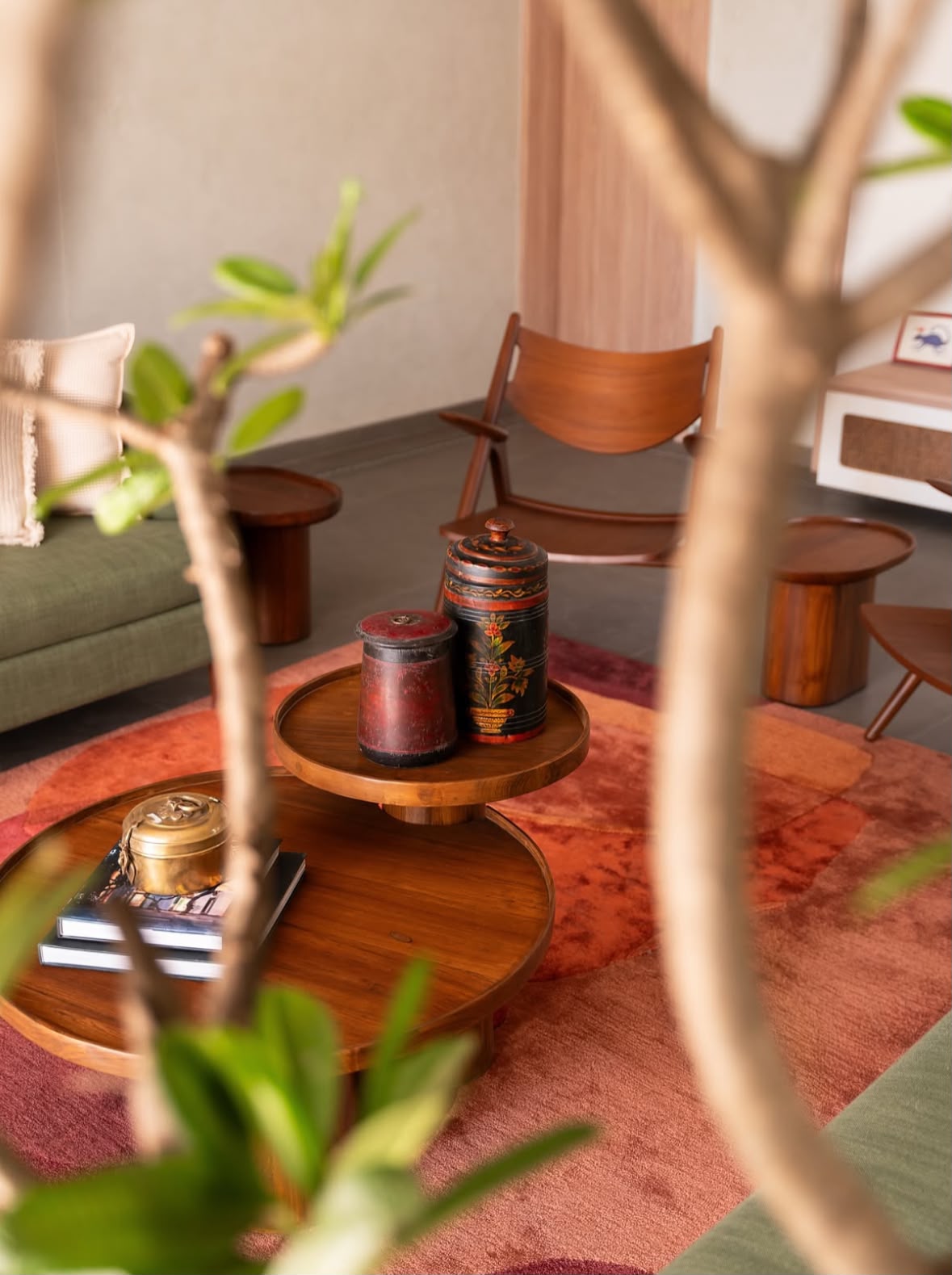 Brass vessels on stacked round tables over a terracotta rug, seen through leaves