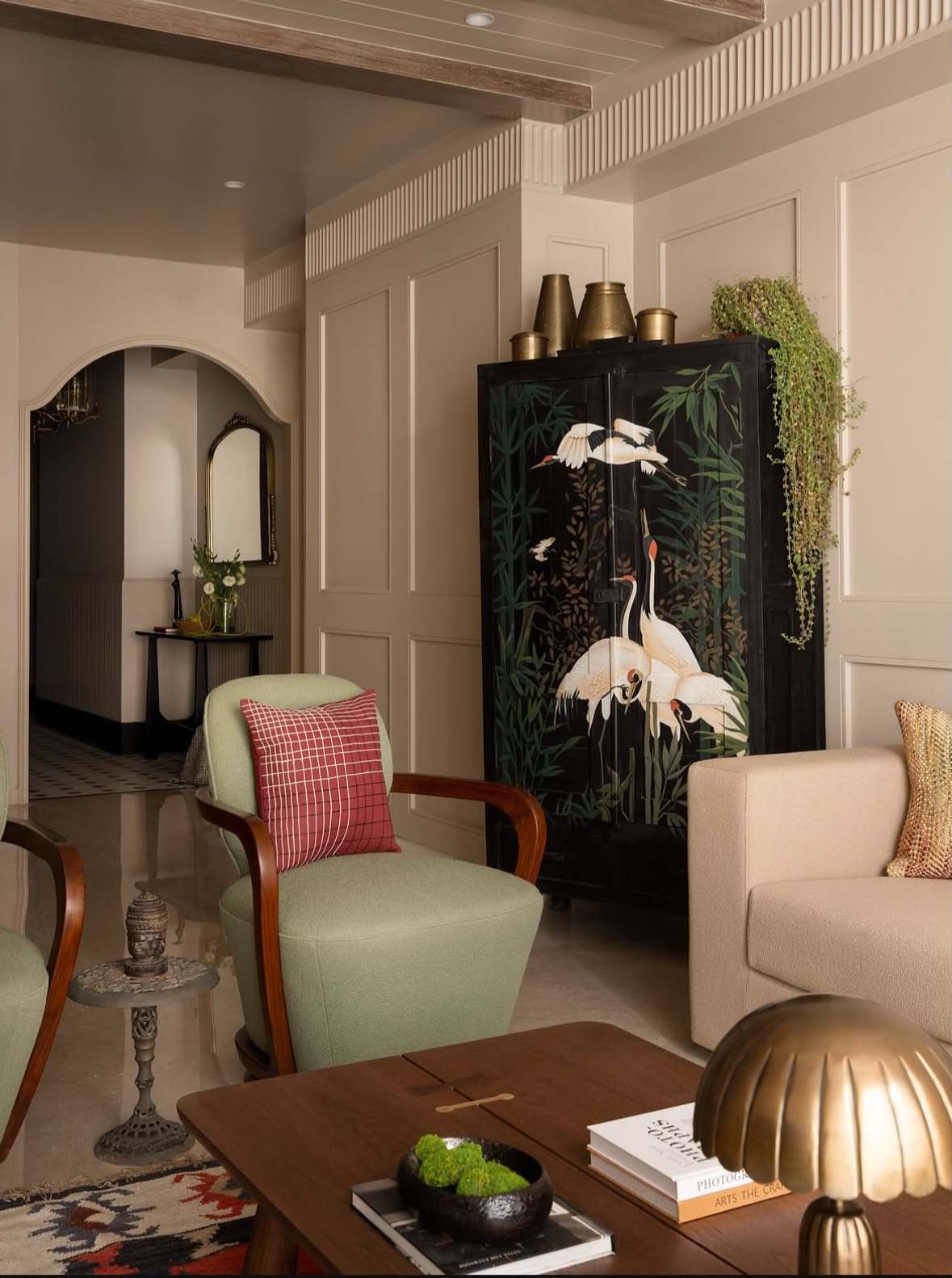 Entrance with a black cabinet painted with white cranes, a green armchair and a brass lamp