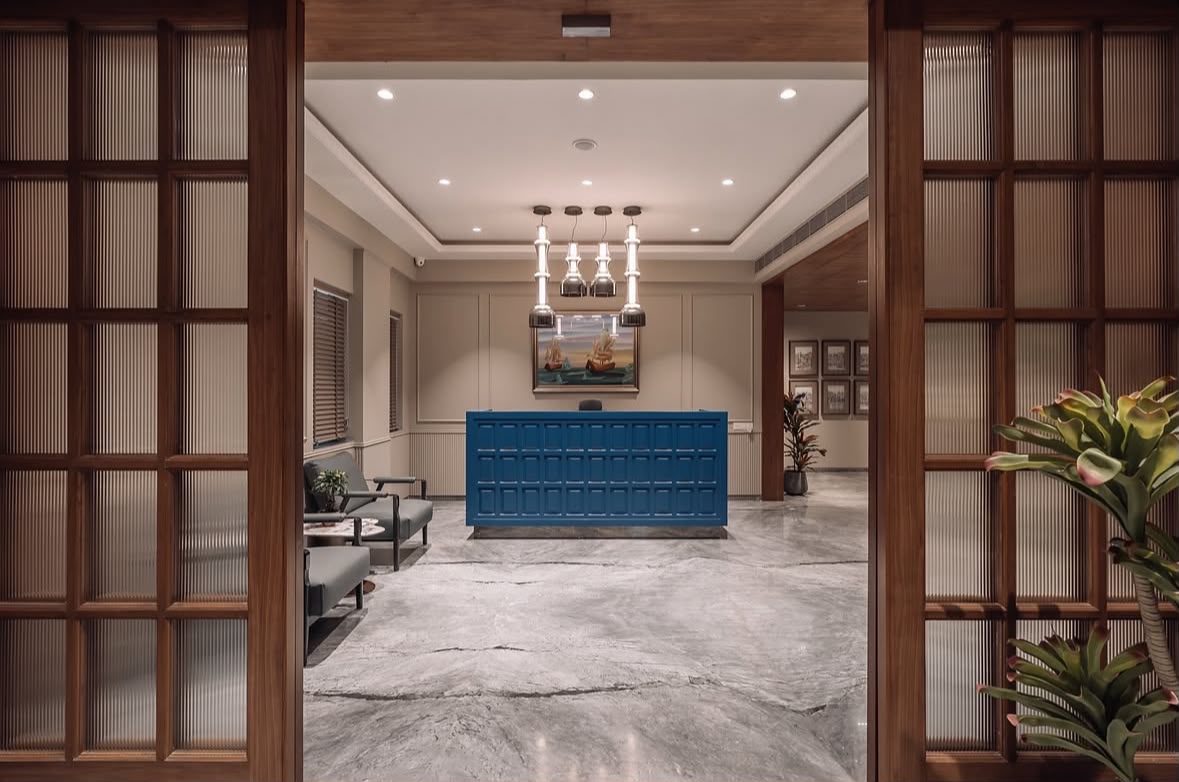 Office reception with a blue panelled desk, pendant lights and grey stone flooring, seen through timber and fluted-glass doors