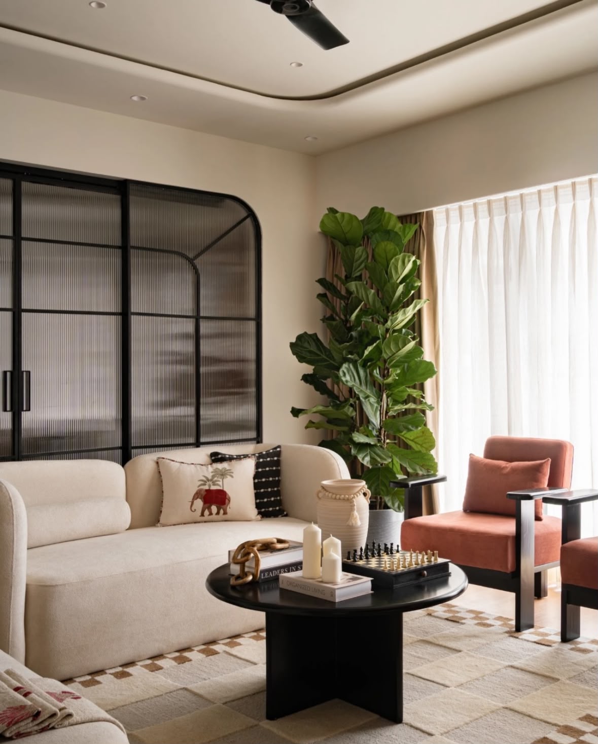 Living room with a cream sofa, rust armchairs, a round black coffee table and a large indoor plant